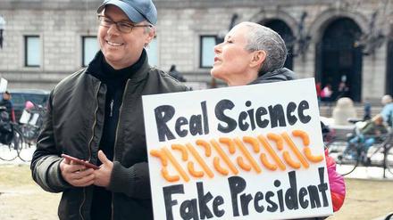 Eine Frau steht auf der Straße mit einem Schild auf der Hand, darauf steht: Real Science, Fake President.