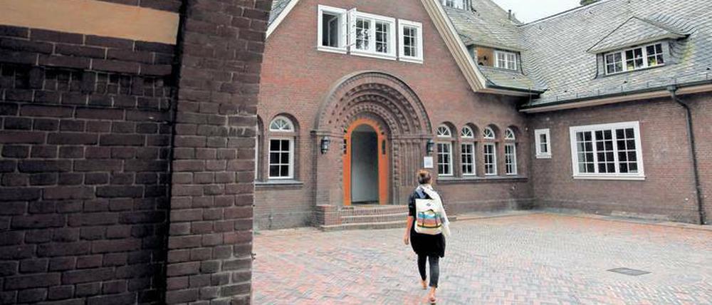 Eine junge Frau mit Rucksack auf dem Rücken geht quer über den Innenhof eines historischen Gebäudes.