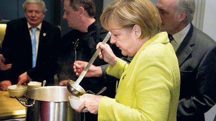 Bundeskanzlerin Merkel füllt in einer Suppenküche eine Schale mit Suppe.