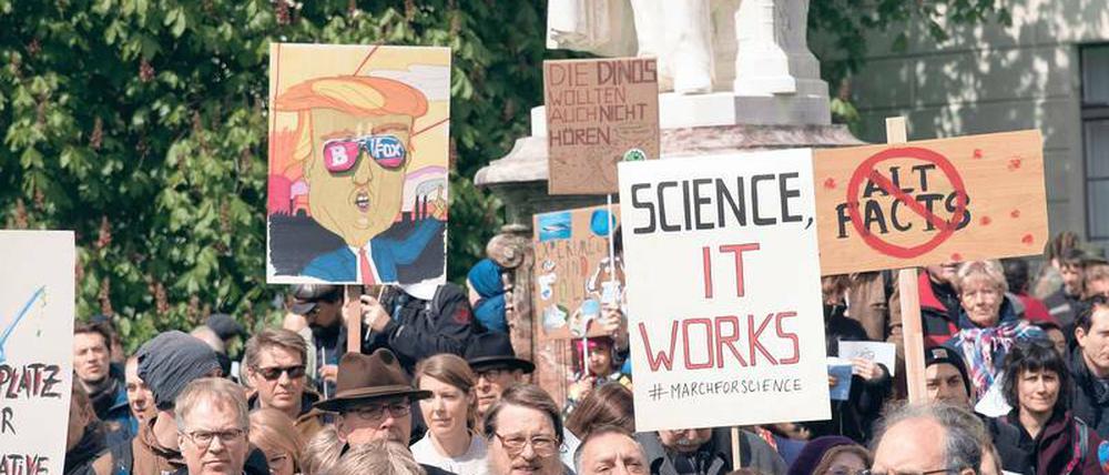 Demonstranten stehen vor einem Universitätsgebäude und halten Schilder hoch mit Aufschriften wie "Science, it works".