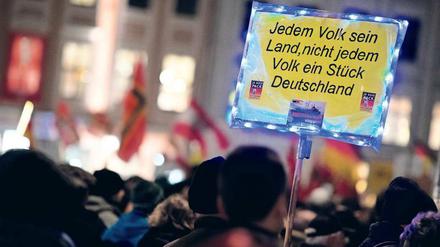 Teilnehmende einer Pegida-Demonstration halten ein Schild mit der Aufschrift "Jedem Volk sein Land, nicht jedem Volk ein Stück Deutschland".