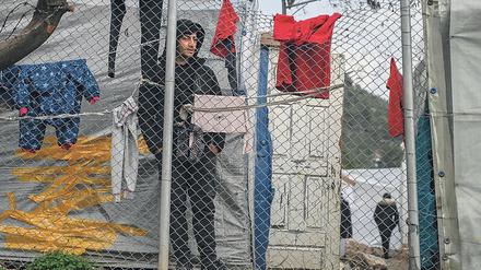 In einem Flüchtlingscamp auf Samos steht ein Mann hinter einem Zaun, an dem Wäschestücke zum Trocknen aufgehängt sind.