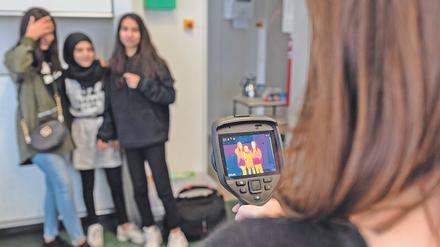 Eine Schülerin macht mit einer Wärmebildkamera eine Aufnahme von drei Mitschülerinnen.