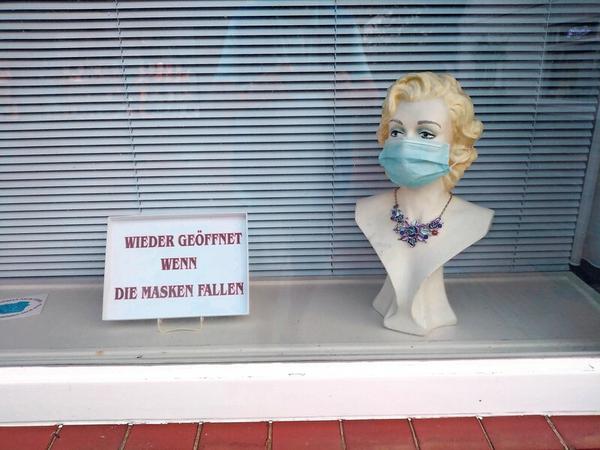 Eine Frauenbüste in einem Schaufenster trägt einen Mund-Nasen-Schutz, daneben steht ein Schild mit der Aufschrift "Wieder geöffnet, wenn die Masken fallen".