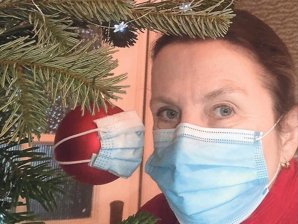 Eine Frau hat sich und eine Kugel an ihrem Weihnachtsbaum mit Mund-Nasen-Schutz fotografiert.