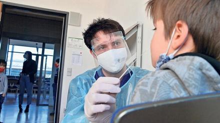 Ein junger Mann mit Schutzmaske und Schutzkleidung nimmt einem Schüler für einen Coronatest aus der Nase eine Probe ab.