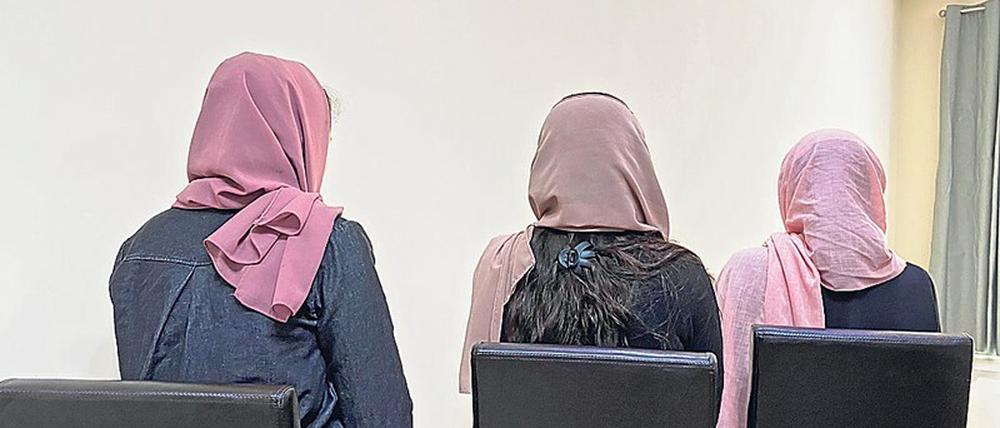 Drei Frauen mit Kopftüchern sitzen mit dem Rücken zur Kamera auf schwarzen Lehnstühlen.