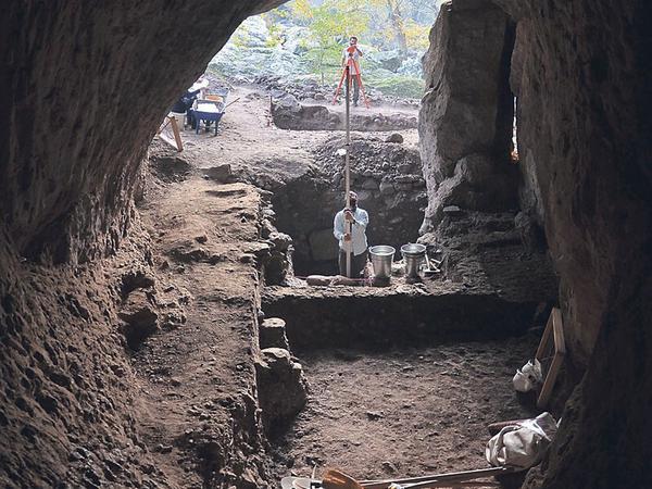In einer Höhle sind Grabungen zu sehen und ein Archäologe, der eine Messung vornimmt.