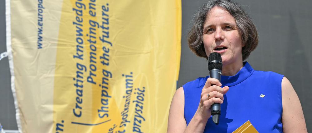 Von Blumenthal steht in einem blauen Kleid vor einem Banner mit blauer Schrift auf gelbem Grund und spricht in ein Mikrofon.