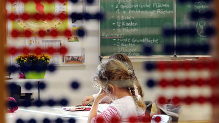 Durch ein Rechenspiel hindurch sind Grundschülerinnen an ihren Tischen im Klassenzimmer zu sehen.