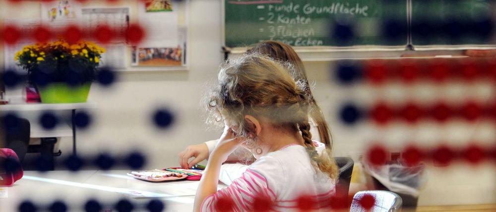 Durch ein Rechenspiel hindurch sind Grundschülerinnen an ihren Tischen im Klassenzimmer zu sehen.