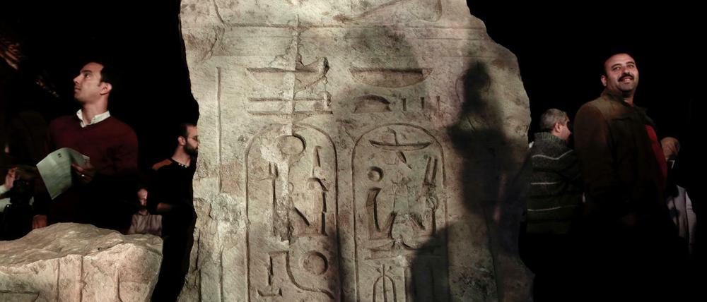 Männer stehen um einen Stein mit Hieroglyphen herum.