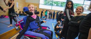 Eine Gruppe von Mädchen, eines sitzt im Rollstuhl, ist lachend in einer Schulturnhalle zu sehen.