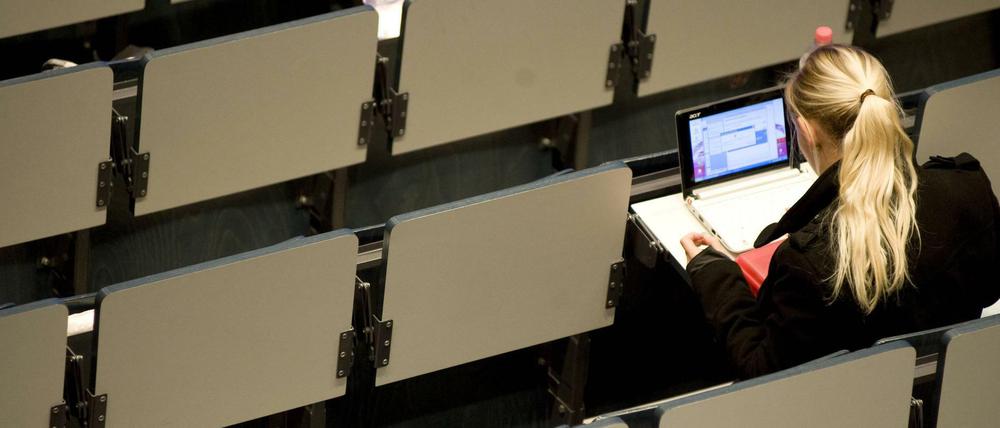 Eine Studentin sitzt alleine in einem Hörsaal und arbeitet an ihrem Laptop.