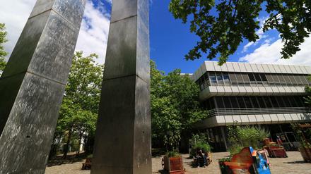 Zwei schwingende Metallsäulen vor einem Unigebäude.