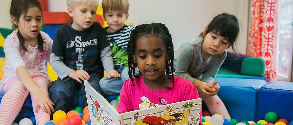 In einer Kita liest ein größeres Kind Kleineren aus einem deutschsprachigen Buch vor.