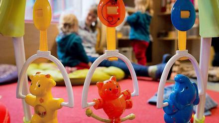 Kleinkinder spielen mit einer Erzieherin, im Vordergrund hängt eine Spielzeugkette.