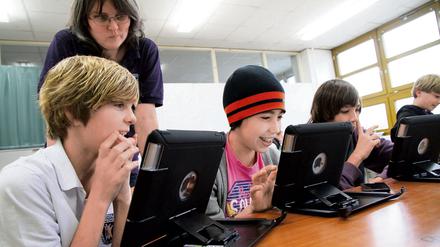 Schüler sitzen in einem Klassenraum vor Tablet-Computern, sie lächeln dabei.