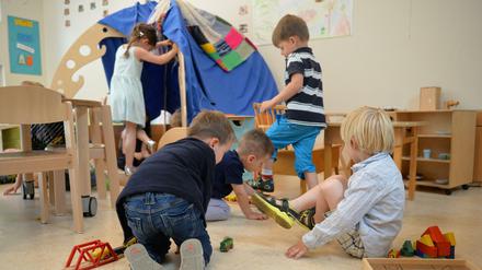 Sieben Kinder spielen in einer Kita mit einer Holzeisenbahn und in einem Zelt.