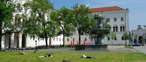 Vor dem historischen Hauptgebäude der LMU München liegen Studierende auf dem Rasen und lesen.