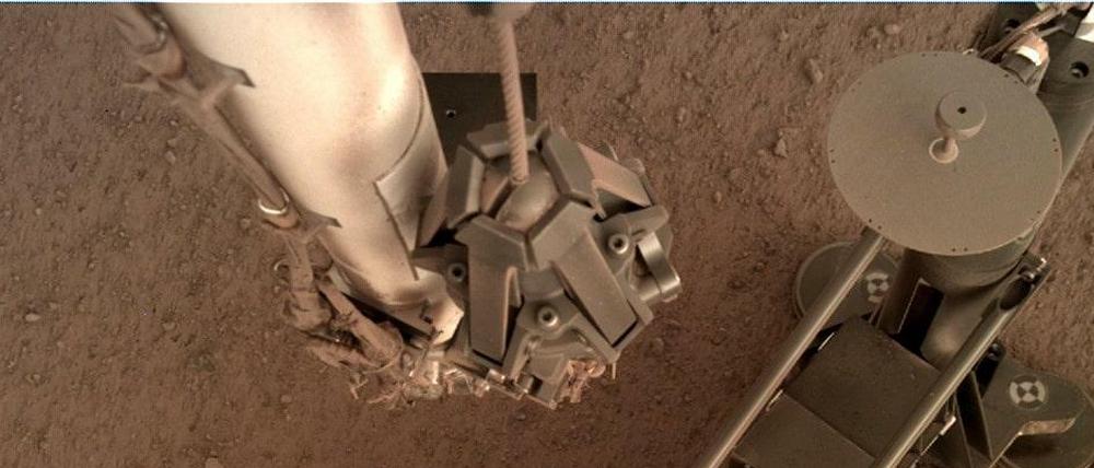 Foto des Marsmaulwurfs, aufgenommen von einer Kamera am Roboterarm der NASA-Sonde "Insight". An den Standfüßen sieht man, wie sich das Gehäuse durch das Hämmern verschoben hat. Die Rammsonde selbst ist rechts oben.