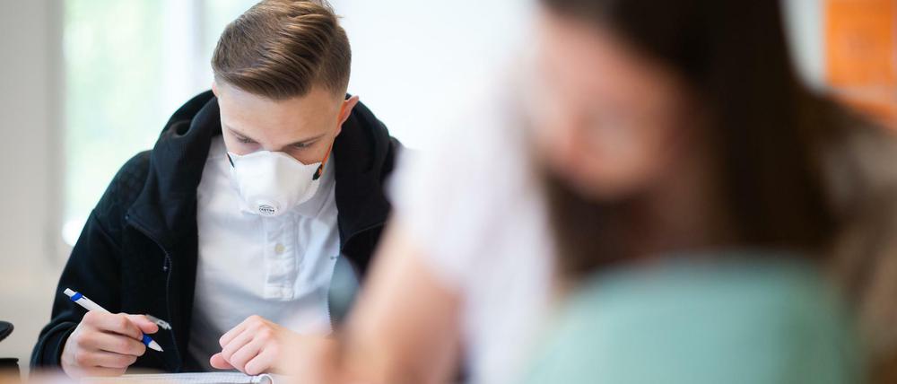 Ein Schüler und eine Schülerin in einer Abiturklasse arbeiten konzentriert im Klassenzimmer, der junge Mann mit Maske.