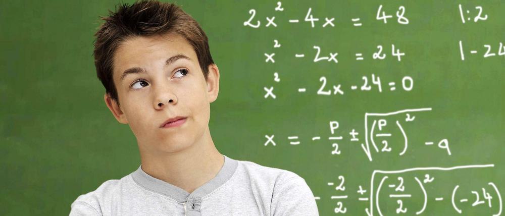 Ein Junge steht vor einer mit Matheaufgaben beschriebenen Tafel.