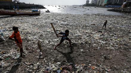 Kinder spielen an einem vermüllten Strand in Mumbai Cricket.