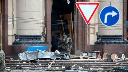 Ukrainische Soldaten und ein Zivilist hantieren vor einem Verwaltungsgebäude in Charkiv mit zerstörten Möbeln.