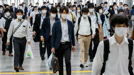 Pendler an einem Bahnhof in Tokio tragen Masken.