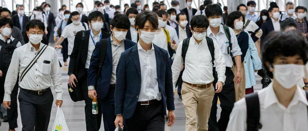 Pendler an einem Bahnhof in Tokio tragen Masken.