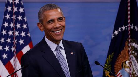 Ex-US-Präsident Barack Obama steht lächelnd vor einer amerikanischen Flagge.