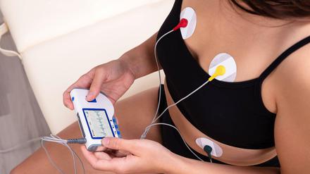 Eine junge Frau überwacht mit Elektroden und Monitor ihren Herzschlag.