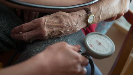 Eine Pflegekraft misst bei deiner Bewohnerin eines Seniorenheims den Blutdruck. Von beiden sind Hände und Unterarme zu sehen.