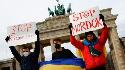 Drei junge Männer halten Schilder u.a. mit der Aufschrift Stop Russian Invasion und eine ukrainische Flagge hoch.