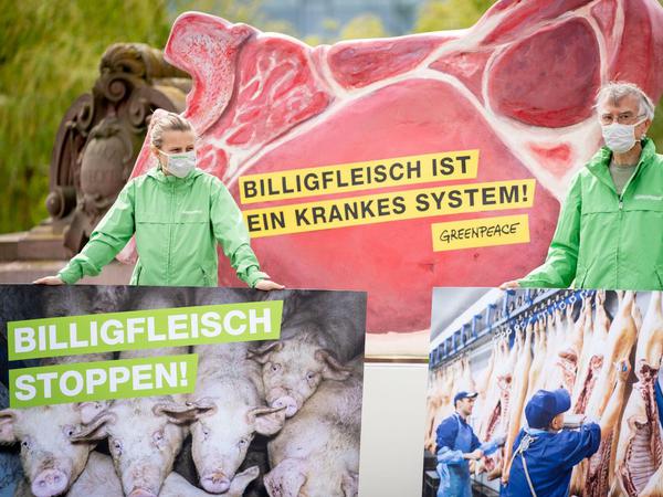 Protestierende zeigen Plakate mit Schweinen kurz vor der Schlachtung und Schweinehälften, die von Arbeitern zersägt werden.