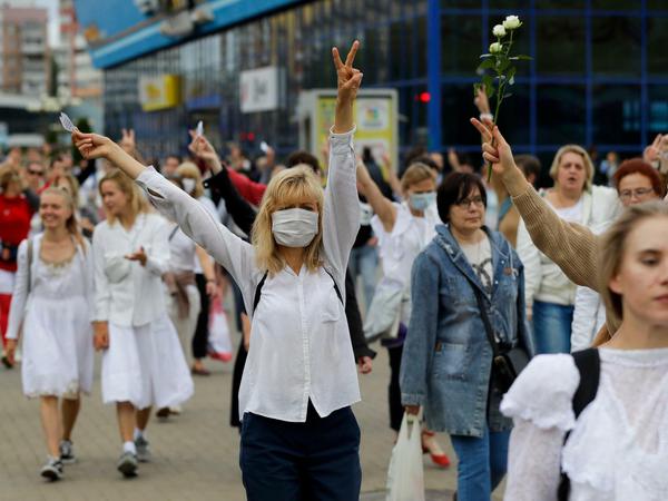 Demonstrantinnen in weißer Kleidung in Minsk machen Peace-Zeichen und halten Blumen in die Luft.