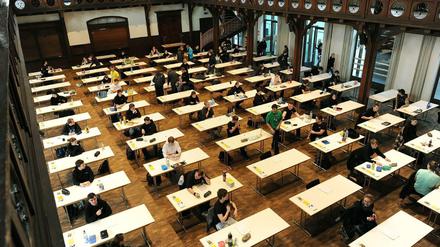 Schüler sitzen bei einer Abiturprüfung in einer historischen Aula an Einzeltischen.