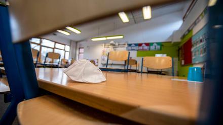 In einem leeren Klassenraum einer Grundschule sind die Stühle auf die Bänke gestellt. Eine Maske liegt auf einem Tisch.