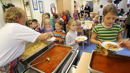 Schülerinnen und Schüler werden in der Mensa einer Grundschule mit Nudeln und Tomatensoße bedient.