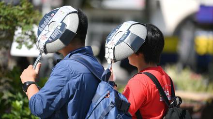 Mit neu gekauften Bratpfannen am Kopf schützen sich zwei asiatische Touristen vor der heißen Sonne bei ihrem Gang durch die Frankfurter Innenstadt.