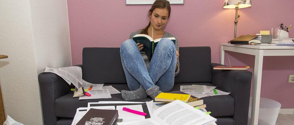Eine Studentin sitzt mit Büchern und kopierten Aufsätzen auf einem Sofa.