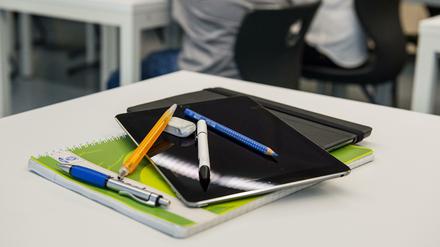 Auf einem Schularbeitstisch liegen ein Tablet-Computer und Stifte auf einem Schulheft.
