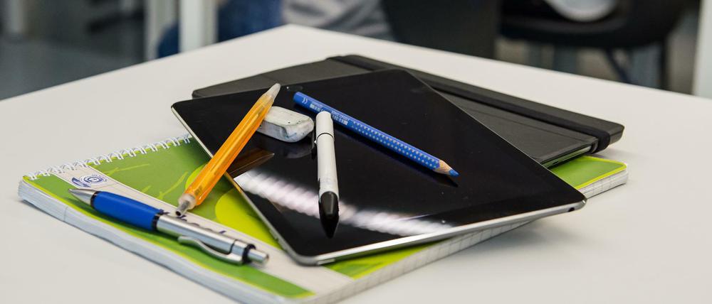 Auf einem Schularbeitstisch liegen ein Tablet-Computer und Stifte auf einem Schulheft.