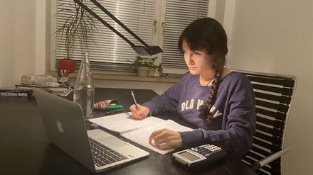 Eine junge Studentin sitzt zu Hause vor ihrem Laptop und schreibt in einem College-Block mit.