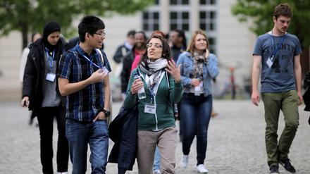 Studierende und Nachwuchswissenschaftler gehen gestikulierend über einen Campus.