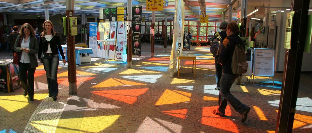 Ein farbiges Glasdach wirft vielfarbige Reflexionen auf den Fußboden einer Eingangshalle, durch die Menschen gehen.