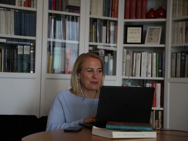 Susanne Zepp sitzt in ihrem Wohnzimmertisch mit Headset vor einem Laptop, neben ihr liegt ein Smartphone.