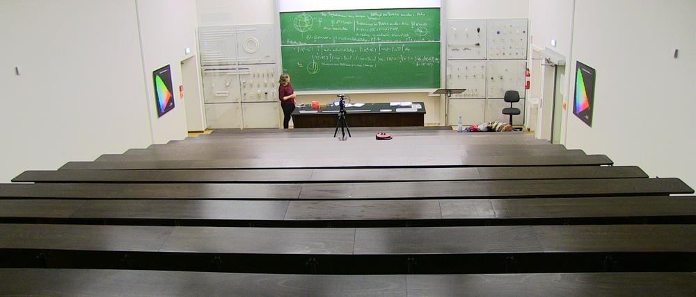 Eine Mathedozentin steht in einem Hörsaal vor einer vollgeschriebenen Tafel. Sie wird bei ihrer Vorlesung gefilmt.
