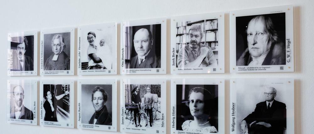 Zwölf Schwarz-Weiß-Porträtfotos historischer Persönlichkeiten sind in einer Zweierreihe an einer Wand angebracht.